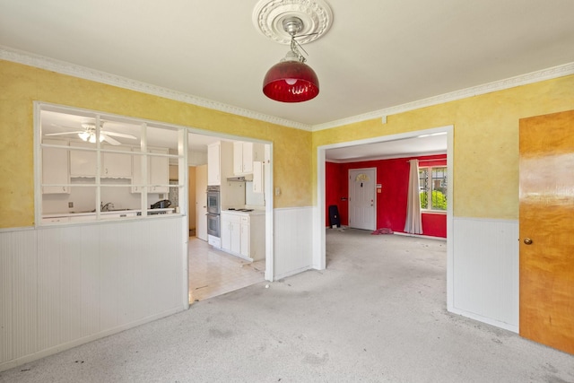 spare room featuring light carpet, a wainscoted wall, a ceiling fan, and crown molding