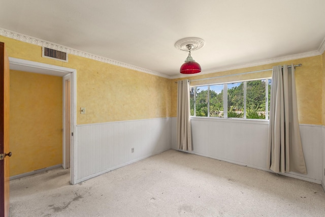 carpeted spare room with visible vents, ornamental molding, and wainscoting