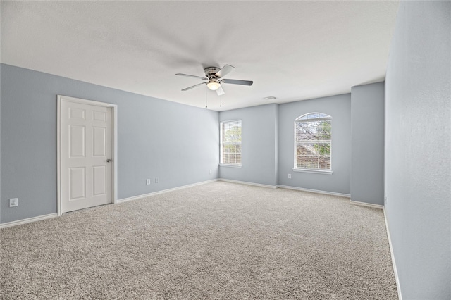 carpeted spare room with visible vents, baseboards, and ceiling fan