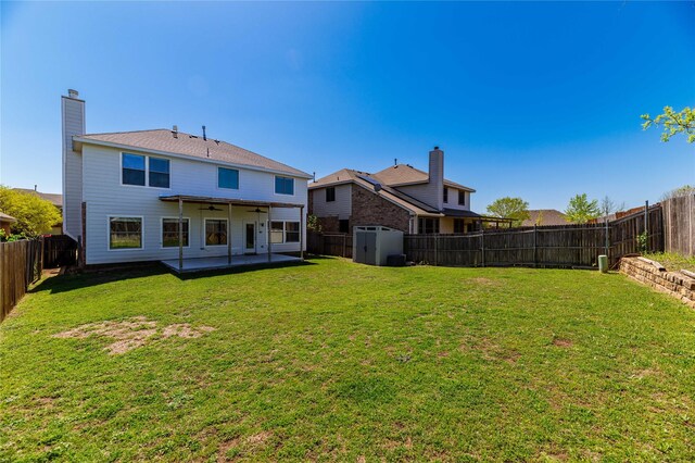 back of property with a storage unit, a fenced backyard, a lawn, ceiling fan, and a patio