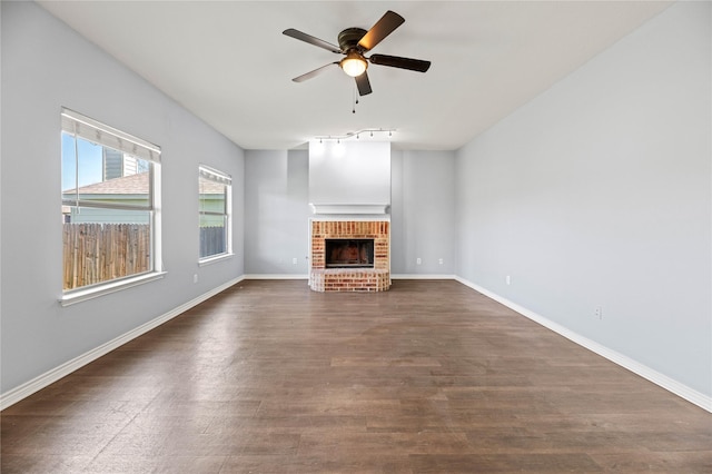 unfurnished living room featuring baseboards, a brick fireplace, a ceiling fan, and dark wood-style floors