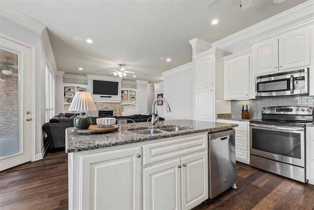 kitchen with dark stone counters, a ceiling fan, a sink, open floor plan, and appliances with stainless steel finishes