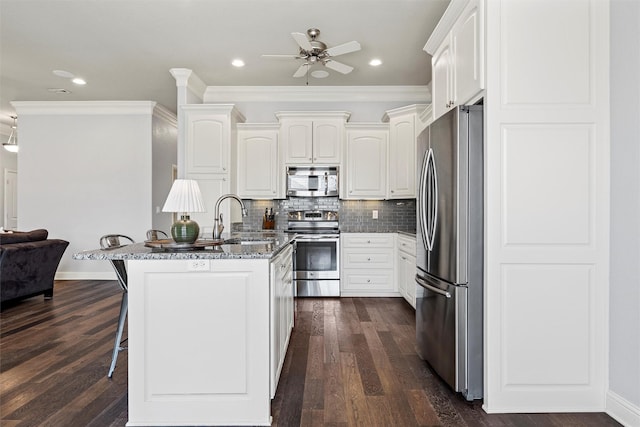 kitchen featuring dark stone counters, a ceiling fan, a sink, a breakfast bar, and appliances with stainless steel finishes