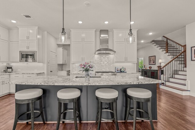 kitchen featuring visible vents, stainless steel microwave, tasteful backsplash, and wall chimney range hood