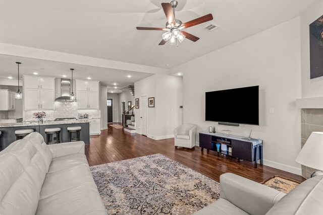 living room featuring stairway, ceiling fan, baseboards, dark wood-type flooring, and visible vents