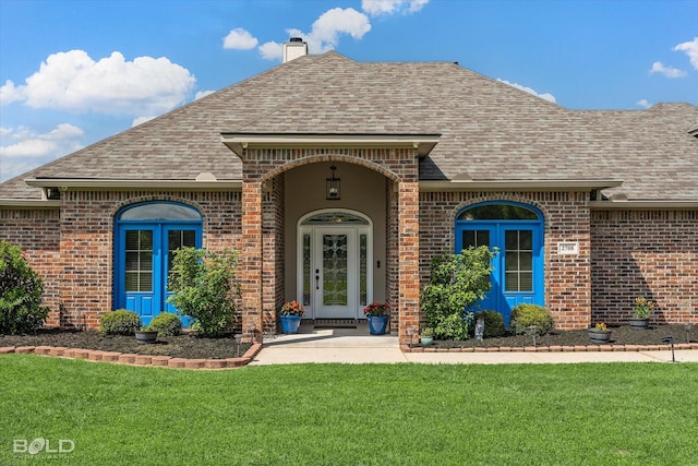 entrance to property featuring brick siding, a lawn, a shingled roof, and a chimney