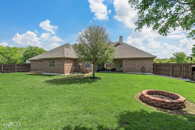 back of property with a fenced backyard, brick siding, an outdoor fire pit, and a lawn