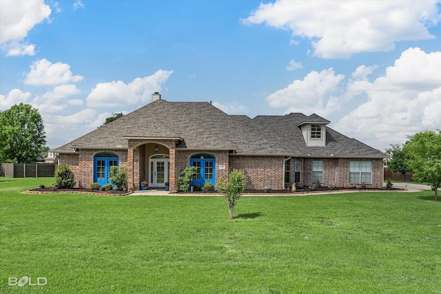 french country inspired facade featuring a front lawn, brick siding, fence, and roof with shingles
