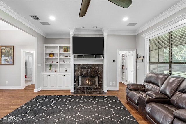 living area featuring crown molding, wood finished floors, ceiling fan, a premium fireplace, and visible vents
