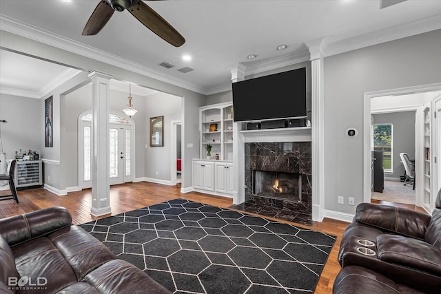 living room featuring wood finished floors, visible vents, ornamental molding, decorative columns, and ceiling fan