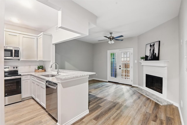 kitchen featuring a peninsula, stainless steel appliances, light wood finished floors, and a sink