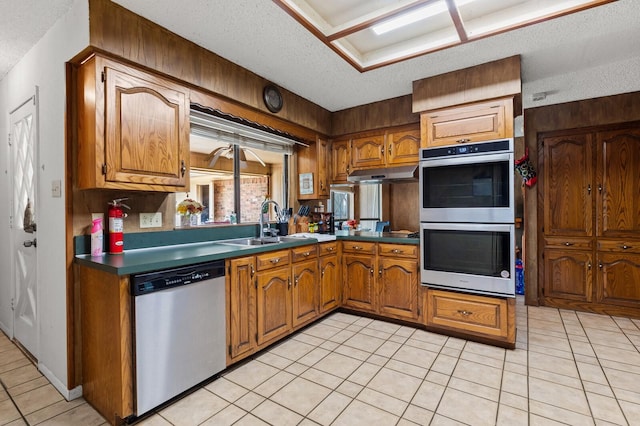 1502 Hinchliffe Rd, Mexia, TX 76667 - kitchen featuring brown cabinetry, a textured ceiling, appliances with stainless steel finishes, and under cabinet range hood