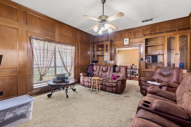 1502 Hinchliffe Rd, Mexia, TX 76667 - carpeted living area featuring a textured ceiling, visible vents, a ceiling fan, wooden walls, and ornamental molding