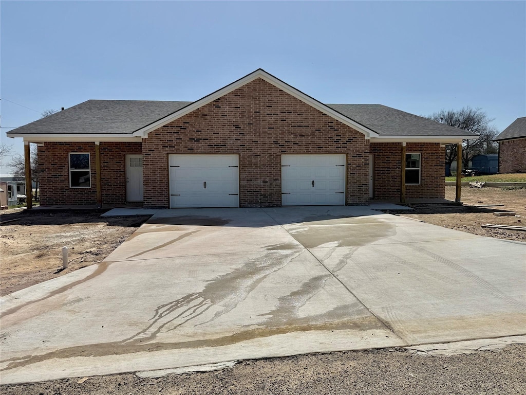 view of front of house featuring brick siding, an attached garage, roof with shingles, and driveway