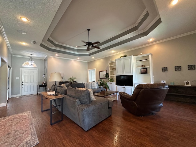 living room featuring dark wood-style floors, a tray ceiling, visible vents, a ceiling fan, and crown molding
