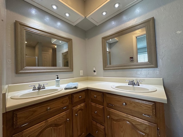 full bathroom featuring double vanity, a textured wall, and a sink
