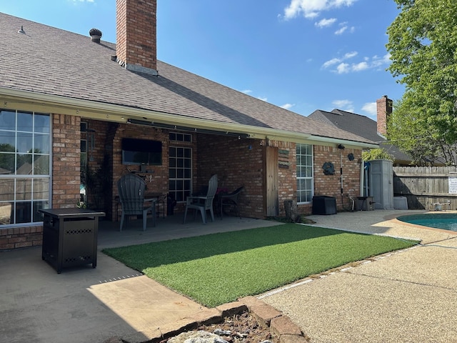 rear view of house featuring a chimney, fence, a patio area, brick siding, and roof with shingles