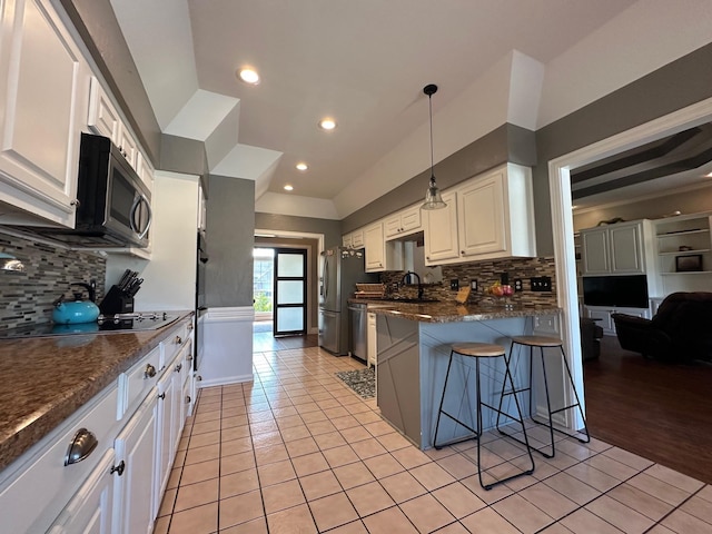 kitchen featuring decorative backsplash, light tile patterned floors, a kitchen bar, white cabinets, and appliances with stainless steel finishes