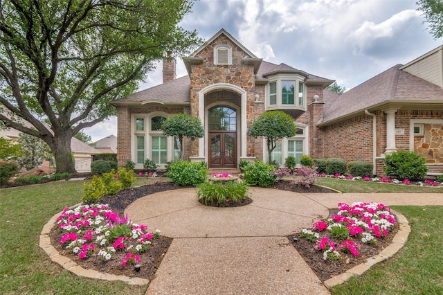 property entrance with french doors, a chimney, brick siding, a shingled roof, and a lawn