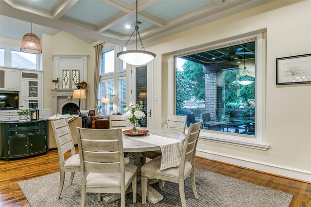 dining room with a fireplace, wood finished floors, beamed ceiling, ornamental molding, and coffered ceiling