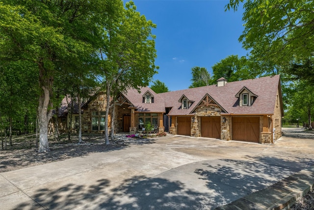 view of front facade with a chimney, an attached garage, driveway, and stone siding