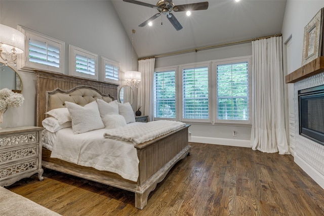 bedroom featuring baseboards, a glass covered fireplace, ceiling fan with notable chandelier, wood finished floors, and high vaulted ceiling