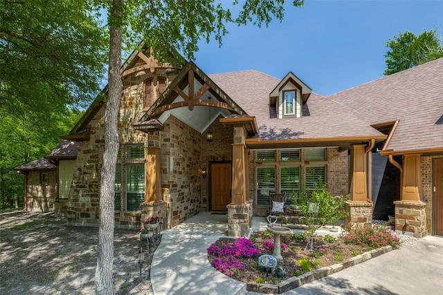 view of front facade with a patio area, stone siding, and a shingled roof