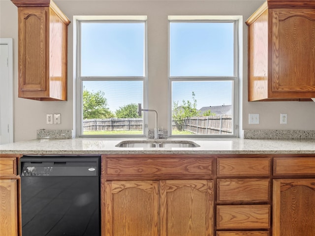 kitchen with light stone countertops, black dishwasher, and a sink