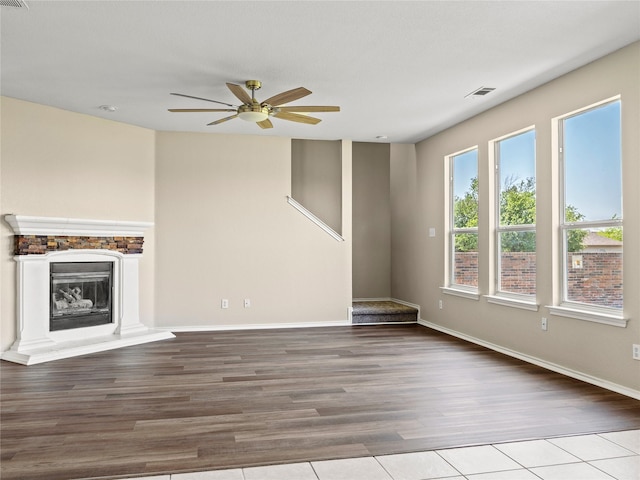 unfurnished living room with wood finished floors, visible vents, baseboards, a glass covered fireplace, and ceiling fan