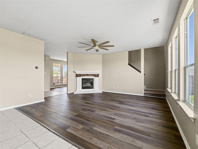 unfurnished living room with a glass covered fireplace, wood finished floors, visible vents, and ceiling fan