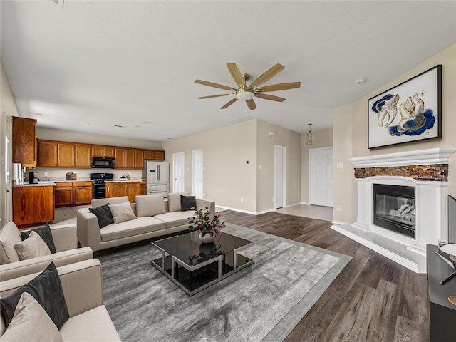 living area with a glass covered fireplace, a ceiling fan, baseboards, and dark wood finished floors