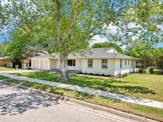 ranch-style house featuring brick siding, an attached garage, a front lawn, and driveway
