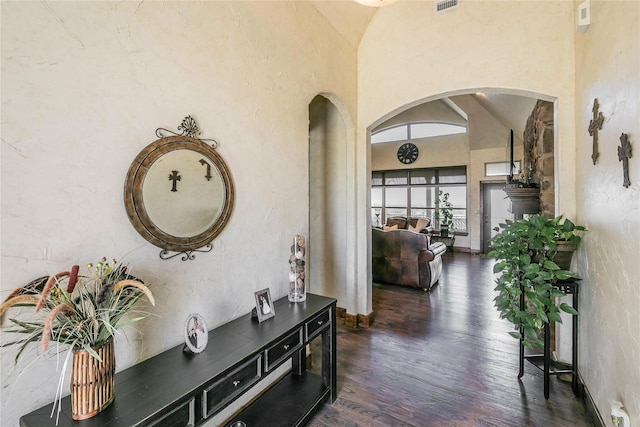 corridor featuring dark wood finished floors, a high ceiling, visible vents, arched walkways, and baseboards