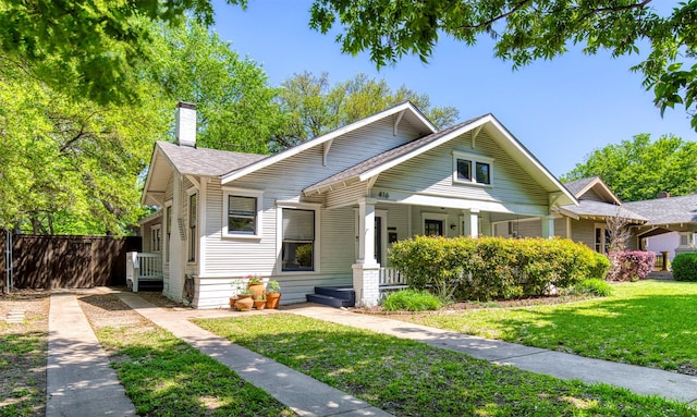 bungalow featuring roof with shingles, a front lawn, a chimney, covered porch, and fence