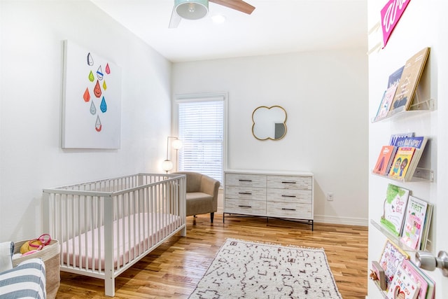 bedroom with wood finished floors, a crib, baseboards, and a ceiling fan