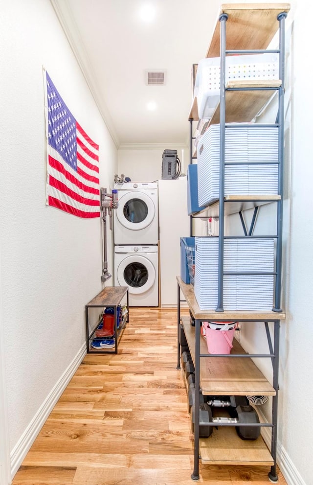 washroom featuring baseboards, crown molding, stacked washing maching and dryer, and laundry area