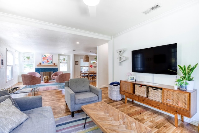 living room featuring crown molding, wood finished floors, a fireplace, baseboards, and visible vents