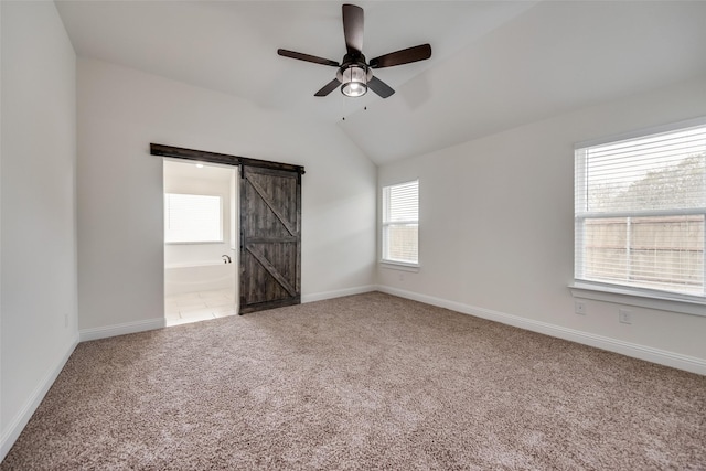 carpeted empty room featuring a barn door, baseboards, vaulted ceiling, and ceiling fan