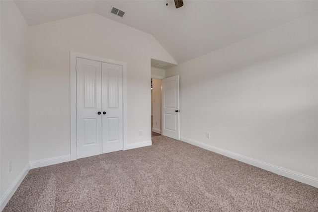 unfurnished bedroom with vaulted ceiling, a closet, carpet floors, baseboards, and visible vents