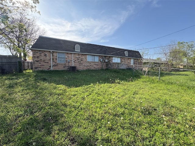 rear view of house featuring brick siding, a yard, a shingled roof, and fence