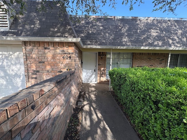 property entrance featuring brick siding and a shingled roof