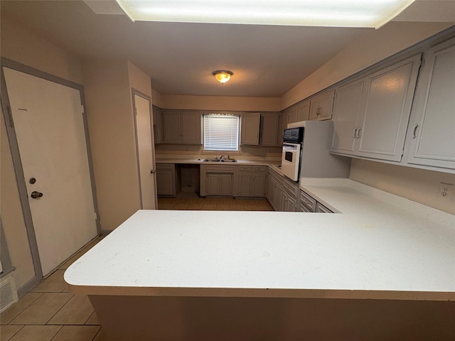 kitchen with a peninsula, light countertops, a sink, and light tile patterned floors