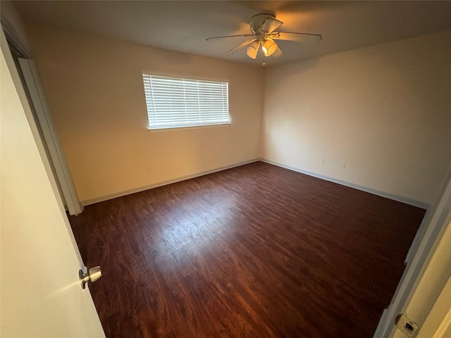 empty room featuring baseboards, a ceiling fan, and dark wood-style floors