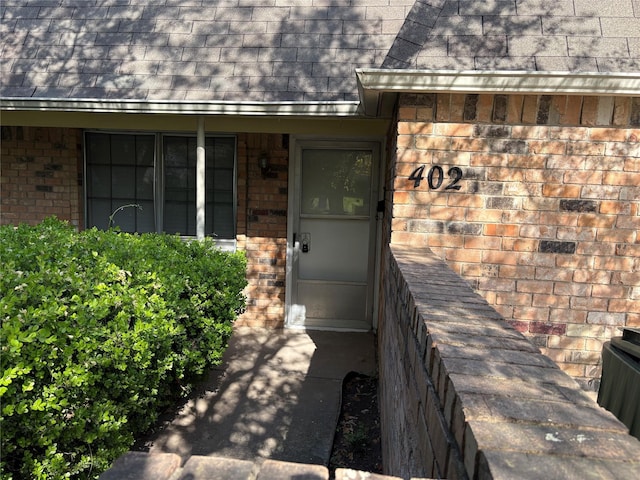 entrance to property featuring brick siding and roof with shingles