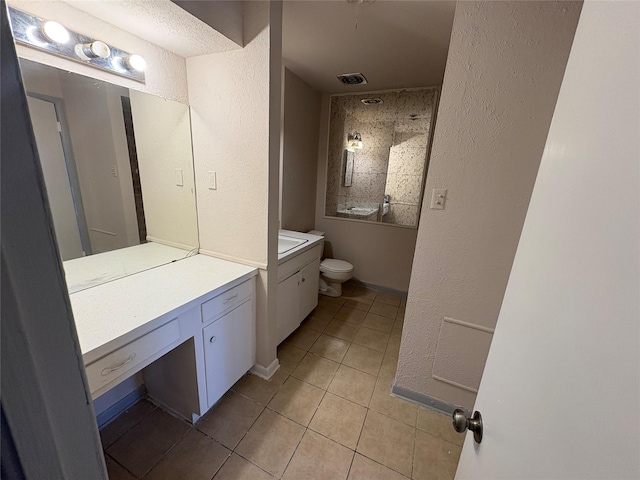 full bath featuring toilet, a textured wall, vanity, and tile patterned floors