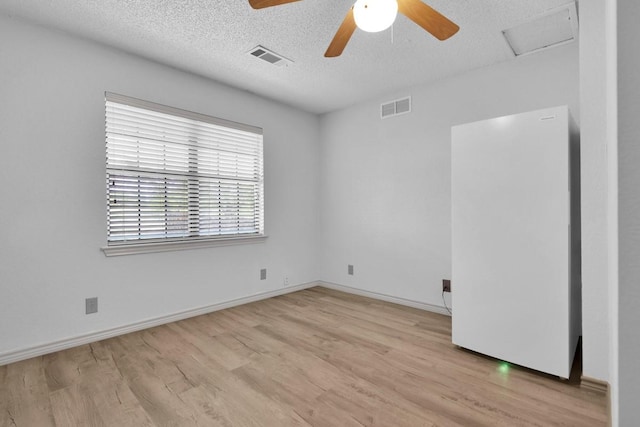 empty room featuring wood finished floors, visible vents, attic access, a textured ceiling, and ceiling fan