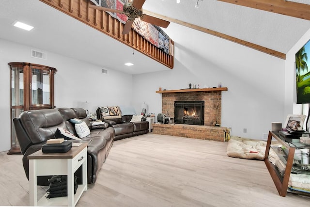 living room with wood finished floors, ceiling fan, beamed ceiling, a brick fireplace, and visible vents