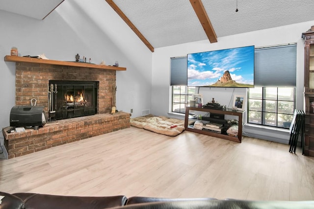 living area with a fireplace, wood finished floors, a textured ceiling, and vaulted ceiling with beams