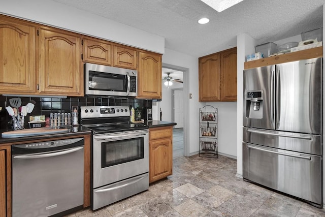 kitchen with stainless steel appliances, dark countertops, decorative backsplash, brown cabinetry, and a textured ceiling