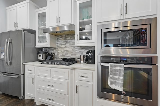 kitchen featuring white cabinets, decorative backsplash, light countertops, under cabinet range hood, and appliances with stainless steel finishes